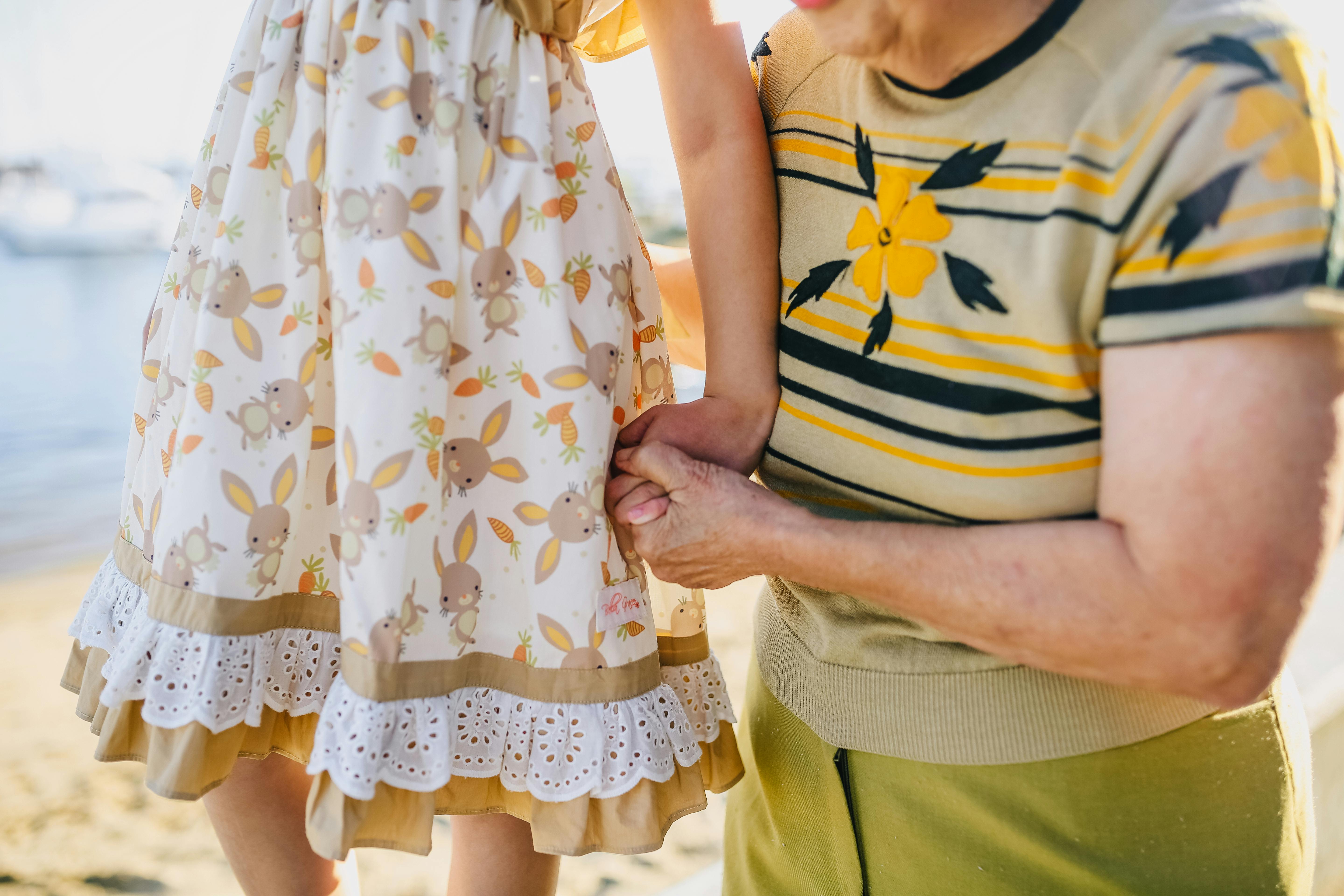An elderly person holding a child's hand on a beach